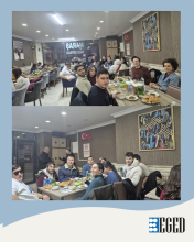 Bir restoranda uzun masalarda oturan kalabalık bir grup insanın bulunduğu iki fotoğraflık bir kolaj. İç mekân aydınlık; tavanda spot ışıklar var ve duvarlarda çerçeveli tablolar asılı.  Üstteki fotoğrafta insanlar yemek masalarında oturuyor; masalarda tabaklar, ekmekler, çorba kâseleri, su şişeleri ve yeşil cam içecek şişeleri bulunuyor. Birkaç kişi kameraya dönük şekilde poz veriyor. Alttaki fotoğrafta başka bir masanın etrafında daha yakın bir grup görülüyor.