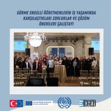Görselde ortada büyük bir grup insan var; otel veya konferans salonunda toplanmışlar. Üstte koyu mavi yazıyla "GÖRME ENGELLİ ÖĞRETMENLERİN İŞ YAŞAMINDA KARŞILAŞTIKLARI ZORLUKLAR VE ÇÖZÜM ÖNERİLERİ ÇALIŞTAYI" yazısı yer alıyor. Grup fotoğrafının ön planında boş sıralar ve ortada yüksek bir yuvarlak masa üzerinde örtü var. Arka planda büyük bir avize, sahne ışıkları ve duvarda çeşitli pankartlar/gösterimler bulunuyor.